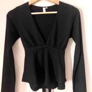 Svart långärmad topp från Nelly - Snygg svart ribbad topp från Nelly med v-ringning och knytning i midjan. Knappt använd och inga defekter.