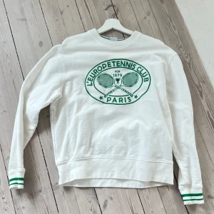 Vit sweatshirt med grönt tryck - Säljer en vit sweatshirt med grönt tryck från L'Europetennis Club Paris. Tröjan har långa ärmar och gröna ränder vid ärmsluten. Perfekt för en sportig look eller en avslappnad dag.💚🫶