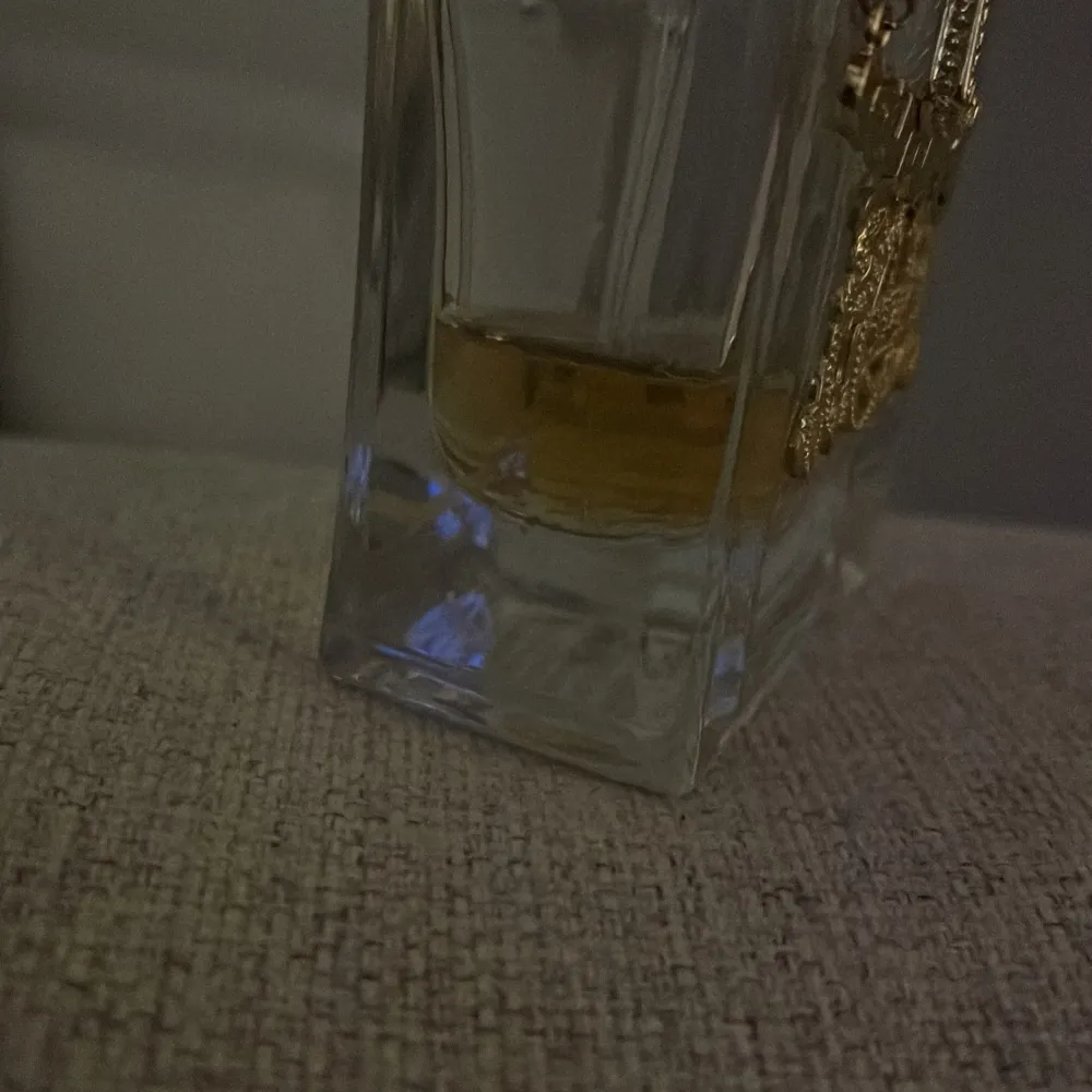 Elegant parfymflaska med en stor rosa rosett och guldfärgad dekor. Flaskan har en fyrkantig form och ett kristalliknande lock. Perfekt för den som älskar lyxiga detaljer och en feminin touch.men har inte så mycket kvar. Perfume.