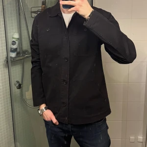 Svart overshirt med knappar - Säljer en stilren svart overshirt med knappar framtill. Jackan har två stora bröstfickor och en klassisk krage. Perfekt för lager-på-lager-stil och passar till många olika outfits. Enkelt och snyggt val för garderoben! 249kr🤗