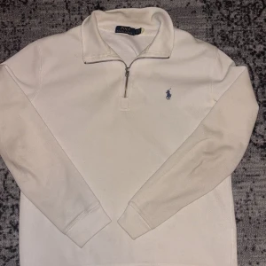 Vit tröja med dragkedja från Polo Ralph Lauren - Säljer en stilren vit tröja från Polo Ralph Lauren med dragkedja och det klassiska logotypbroderiet på bröstet. Perfekt för en avslappnad men ändå snygg look. Tröjan har långa ärmar och en bekväm passform.
