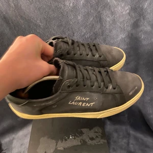 Svarta sneakers från Saint Laurent - Snygga svarta sneakers från Saint Laurent med vit logga på sidan. 9/10 skick✅  men den håller i den har lossnat lite där fram på ena skon Storlek 41✅ Allt på bild fem följer med ✅🤑Skriv om ni har frågor eller funderingar priser är inte hugget i sten. Köpta av alle på TikTok privat. Såklart äkta❤️✅