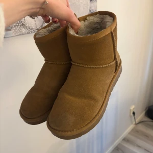 Uggs liknande skor  - Säljer ett par mysiga bruna boots med mjukt foder. Perfekta för kyliga dagar med sin varma insida. De har en enkel design utan snörning och är lätta att ta på och av.
