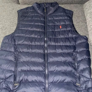 POLO RALPH LAUREN VÄST  - Säljer en snygg mörkblå dunväst från Ralph Lauren med dragkedja, den är använd bara ett fåtal gånger men har inga problem med västen och inga skador finns på västen, ny pris 3600 passar även till XL