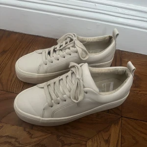 Beiga sneakers från Zara - Snygga vita sneakers från Zara med klassisk design och snörning. Perfekta för en stilren look. Tillverkade i syntetmaterial med en bekväm passform. Använda någon gång, fläck på insida hälen (se bild).