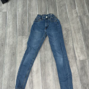 Blå jeansbyxor från Snake Star - Snygga blå jeansbyxor från Snake Star med hög midja och skinny passform. Byxorna har klassisk femficksdesign och stängs med dragkedja och knapp. Perfekta för en stilren look.