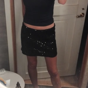 Svart glittrig kjol - Snygg svart kortkjol med paljetter som ger en glittrig look. Perfekt för att sticka ut på festen. Kjolen har en tight passform och är tillverkad i ett syntetmaterial som ger en bekväm känsla.