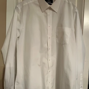 Vit skjorta från Lapidus - Klassisk vit skjorta från Lapidus i storlek 42. Skjortan är långärmad och har en bröstficka. Den är tillverkad i ett non-iron material vilket gör den lättskött och perfekt för en stilren look. Perfekt för både formella och avslappnade tillfällen.