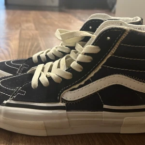 Marinblå vans med vit snörning - Säljer ett par klassiska marinblå Vans sneakers med vit snörning och vit sula. Skorna har en hög modell med vit sidostrip. Nästan aldrig använda, endast en gång. Super bra skick som nya! 