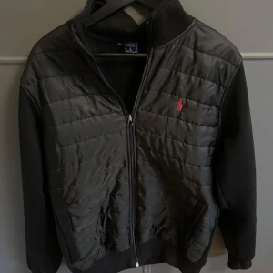 Svart cardigan från Ralph Lauren  - Säljer en svart jacka från Ralph Lauren med quiltad framsida och dragkedja. Jackan har en broderad logotyp i rött på bröstet och långa ärmar. Perfekt för en stilren look, säljs i j i butik längre och det ör riktigt bra skick på den. Hör av er vid minsta fundering… pris kan diskuteras vid snabb affär 😁