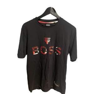 Säljer en svart t-shirt från Boss med Chicago Bulls-logga som inte säljs längre!. T-shirten har korta ärmar och är perfekt för vardagsbruk eller sportevenemang. Den är i bra skick och har en cool design med texten 'BOSS' i ett mönster som matchar Bulls färger.