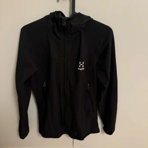 Svart vindjacka från Haglöfs - Säljer en svart vindjacka från Haglöfs i storlek S för damer. Jackan har en dragkedja framtill och två fickor med dragkedjor. Den har en huva och är långärmad. Perfekt för utomhusaktiviteter under vår och höst.
