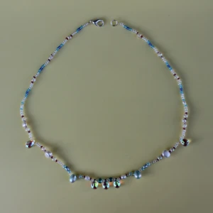 Färgglatt pärlhalsband - Säljer ett superfint och färgglatt pärlhalsband. Halsbandet har små pärlor i olika färger som blått, vitt och rött, samt några större pärlor som skimrar i regnbågens färger. Perfekt för att liva upp vilken outfit som helst! 💖