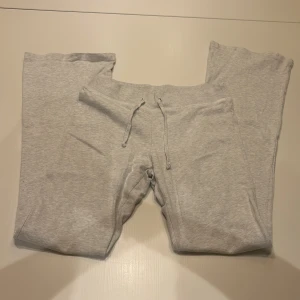 Grå mjukisbyxor från Brandy Melville - Säljer ett par lågmidjade, figurnära grå mjukisbyxor från Brandy Melville. De är i Onesize men passar som en XS/S/M och har en bekväm passform med snörning i midjan. Perfekta för en chill dag hemma eller en avslappnad promenad.