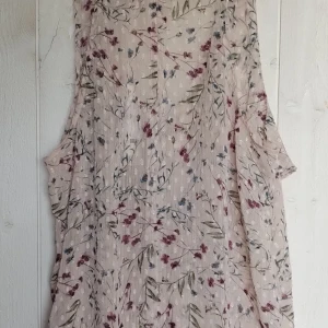 Blommig kortklänning med knytning - Säljer en ny superfin blommig kort volang blus i ljusa toner. linneblusen har ett vackert blommönster i rött, blått och grönt på en beige bakgrund. Den är ärmlös och har 2 knappar framtill. Perfekt för sommarens alla fester under eller en mysig dag på stan!