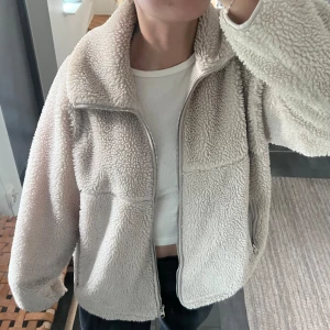 Beige teddyjacka från Arket - Säljer en supermysig beige teddyjacka från Arket med dragkedja framtill. Jackan har en hög krage och långa ärmar, perfekt för kyliga dagar. Den är i mycket fint skick!! Perfekt för höst och vinter!! Storlek S 🎀nypris 1150 kr och helt slutsåld!!