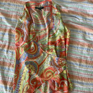 Färgglad omlottklänning från Lauren Ralph Lauren - Säljer en superfin och färgglad topp från Ralph Lauren i storlek XS. Klänningen har ett härligt paisleymönster i orange, grönt, blått och gult. Den är ärmlös och har en v-ringad hals. Perfekt för sommarens alla fester! 🌸