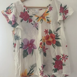 En tröja - Tröjan är vit med blommor på, precis som på bilderna. Gjord av ett tunnt material. Tillverkad i Vietnam. 