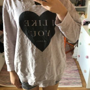 Grå tröja med text - Säljer en grå tröja med texten 'I LIKE YOU (A LOT)' tryckt i ett svart hjärta på framsidan. Tröjan är långärmad och har en avslappnad passform. Perfekt för en mysig dag hemma eller en avslappnad dag ute. Tröjan är i bra skick och väldigt bekväm att ha på sig.