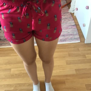 Rosa shorts med ananasmönster - Säljer ett par supergulliga rosa shorts från H&M med ananasmönster. De är i storlek S och har en bekväm midwaist passform. Shortsen har en knytning i midjan och är perfekta för sommarens varma dagar. Materialet känns mjukt och skönt mot huden. Perfekta för både chill och fest! Kan också användas som pyjamas. Har använt den mycket så den är inte ny 🩷