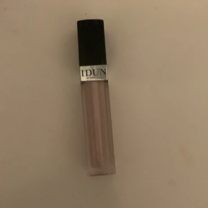 Läppglans från IDUN Minerals - Säljer ett superfint läppglans från IDUN Minerals. Det är i en snygg, neutral nyans som passar perfekt till vardags eller fest. Läppglanset kommer i en genomskinlig tub med svart lock och IDUN-loggan på framsidan. Det är lätt att applicera och ger en fin glansig finish. Perfekt för att ge dina läppar lite extra glans och färg!
