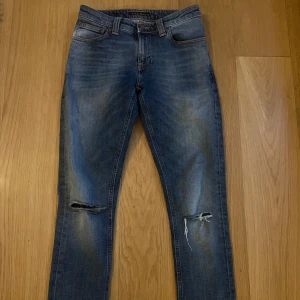 Blå jeans från Nudie Jeans W27 L34 - Säljer ett par snygga blå jeans från Nudie Jeans i bra skick. De har en cool slitning på knäna och klassisk femficksdesign. Perfekta för en avslappnad stil! 🕶️skicket på Jeansen är 5,5/10 skick öppen till frågor👏