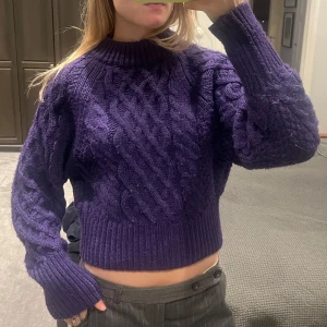 Mörklila stickad tröja - Säljer en superfin mörklila stickad tröja med flätmönster från hm. Den är croppad och har långa ärmar, perfekt för höst och vinter. Tröjan är både mysig och stilren, passar till både jeans och kjol. Perfekt för att hålla sig varm och snygg! 💜