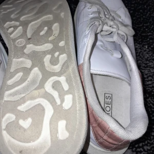 Vita sneakers med rosa detaljer - Säljer ett par vita sneakers från M Shoes i bra skick. De har snygga rosa detaljer på hälen och klassisk snörning. Perfekta för vardagsbruk och ger en stilren look. Sulan har ett unikt mönster som ger bra grepp.