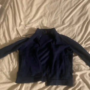 Blå träningsjacka från adidas - Säljer en blå träningsjacka med dragkedja och vita ränder längs ärmarna. Perfekt för sportiga aktiviteter eller som en casual vardagsjacka. Den har en bekväm passform och är i bra skick. Passar perfekt för höst och vår!