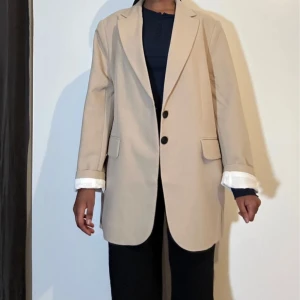 Beige kavaj - Snygg beige kavaj i normal passform. Perfekt för både vardag och fest. Den har långa ärmar och stängs med två knappar framtill. Klassisk och stilren design som funkar till allt! Den är oanvänd 