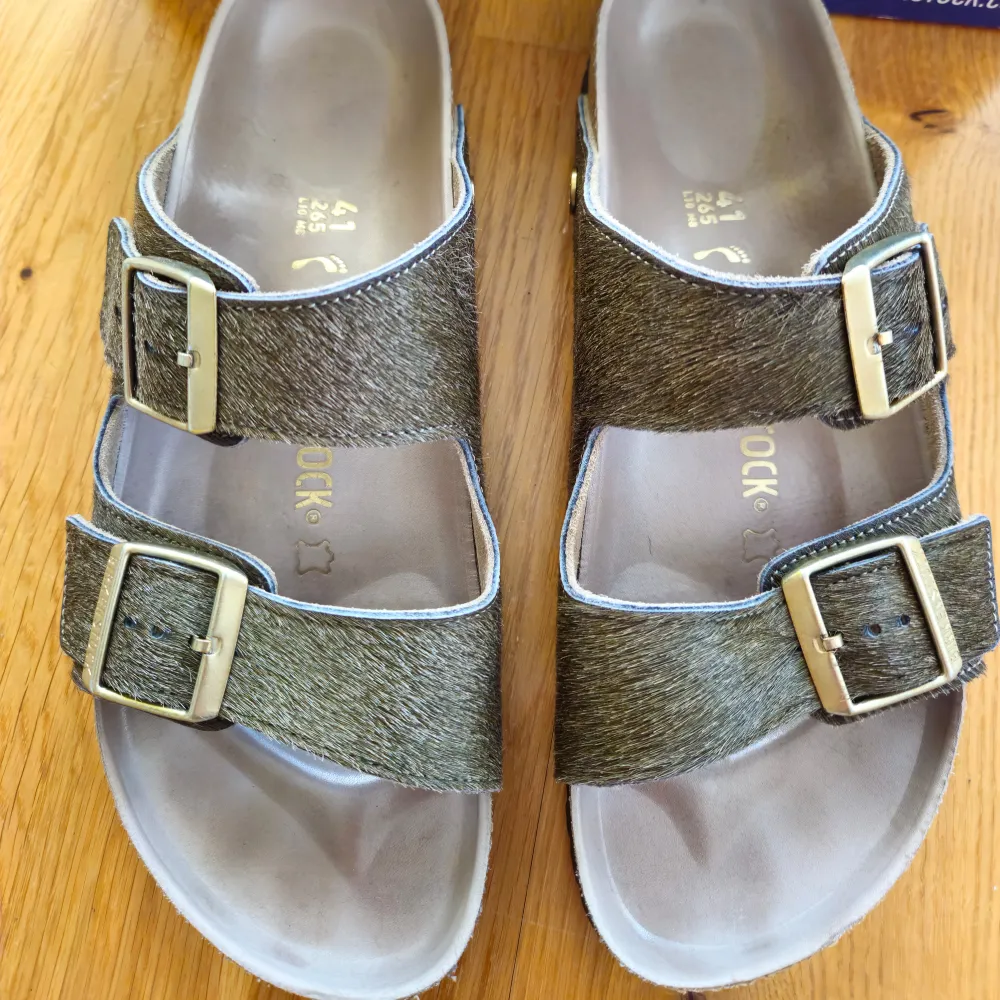 These Birkenstock Arizona Rivet Logo sandals are in the color Olive Melange. They are in perfect condition. Size: 41, narrow fit. Real fur on top.. Skor.