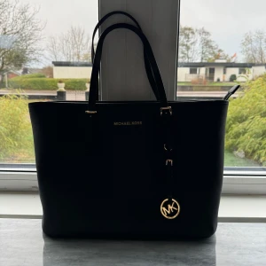 Svart väska från Michael Kors - Säljer en elegant svart handväska från Michael Kors i mycket bra skick. Väskan har en stilren design med guldiga detaljer och ett klassiskt MK-hänge. Perfekt för både vardag och fest! 🖤 det finns små repor på hänget, kolla bild nr 3. Inget som man tänker på eller lägger märke till och syns inte tydligt från långt avstånd. Själv får jag plast med mitt cykelbatteri och skoldator i den.  Nypris: Ca 3000kr. Finns lite små vita repor på väskan, inget som är jättetydligt men skriv för fler bilder. 