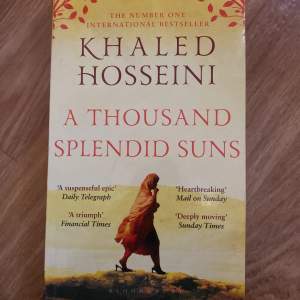 Säljer boken 'A Thousand Splendid Suns' av Khaled Hosseini. Det är en internationell bästsäljare med ett omslag som visar en person i röd klädsel mot en gul bakgrund. Perfekt för dig som gillar gripande och känslosamma berättelser.