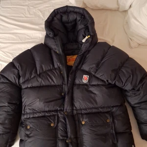 Svart dunjacka från Fjällräven - Säljer en svart dunjacka från Fjällräven i mycket bra skick. Jackan har en mysig huva och praktiska fickor med knappar. Går utmärkt att ställa in efter kroppen, passar från XXS-L då den går o ställa in. Den ända defekten på jackan är den lilla vita fläcken på sidan och en liten på fläck på insidan som är mycket liten. Jag vet inte hur vida fläckar går bort då jag inte testat! Därav så ligger priset där det gör. Utöver det så är jackan helt i nyskick då den är använd sparsamt🖤
