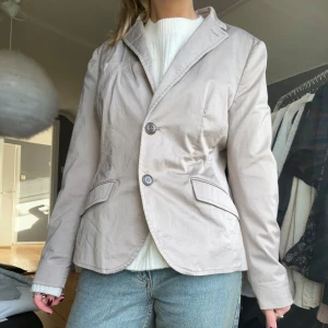 Beige kavaj med knappar - Säljer en stilren beige kavaj med två knappar framtill. Perfekt för både vardag och fest. 