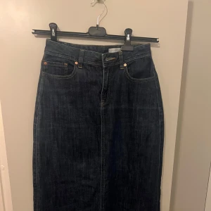 Mörkblå jeanskjol från Jeanswest - Säljer en snygg mörkblå jeanskjol från Jeanswest. Kjolen är i lång modell och har en klassisk femficksdesign. Perfekt för både vardag och lite mer avslappnade tillfällen. Den är i mycket bra skick