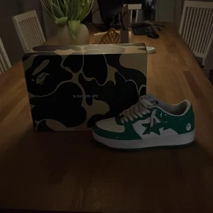 Gröna och vita sneakers från A Bathing Ape - Säljer ett par snygga gröna och vita sneakers från A Bathing Ape. Skorna har en stjärndetalj på sidan och kommer med originalkartong. Perfekta för att ge din outfit en cool touch! De är i mycket bra skick och har klassisk snörning.