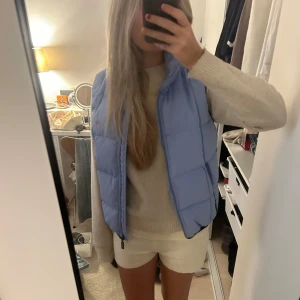 Ljusblå dunväst - Säljer en ljusblå dunväst i mycket bra skick. Västen är quiltad och har en dragkedja framtill. Perfekt för höst och vår när du vill hålla dig varm.