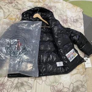 Svart dunjacka från Moncler - Säljer en snygg svart dunjacka från Moncler i nytt skick. Jackan är pufferstil med en glansig finish och har en praktisk dragkedja framtill. Den är långärmad och perfekt för vintern. Storleken är inte specificerad, men den ser ut att vara normal passform. Perfekt för att hålla sig varm och stilren i kylan!