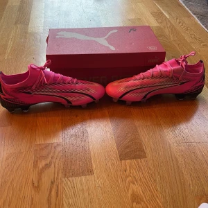 Puma Ultra Match FG/AG i Poison Pink - Säljer ett par Puma Ultra Match FG/AG fotbollsskor i en cool poison pink färg med svarta och vita detaljer. Skorna är i nytt skick och kommer med originalkartong. Perfekta för både gräs och konstgräs. Skorna har snörning för en säker passform. Perfekta för dig som vill sticka ut på planen! ⚽️