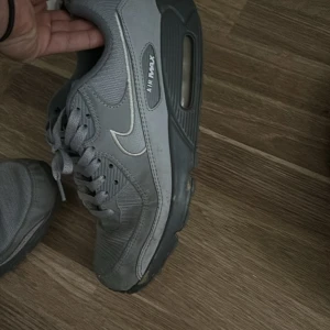 Grå Nike Air Max sneakers - Säljer ett par grå Nike Air Max sneakers i bra skick. De har en klassisk design med snörning och synlig Air Max-dämpning i sulan. Perfekta för vardagsbruk och ger en skön känsla vid varje steg. Några tecken på användning finns, men de är fortfarande i gott skick.