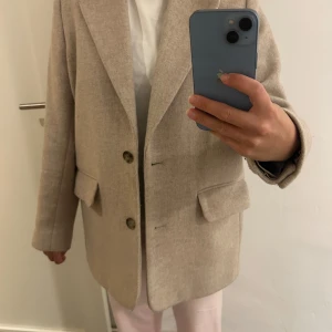 Beige kavajkappa från & Other Stories - Säljer en oversized beige kavaj från & Other Stories i ull. Den har en klassisk design med två knappar och fickor fram. Perfekt för både höst och vår. Kavajen är i mycket bra skick men har några små defekter. Nypris 2000