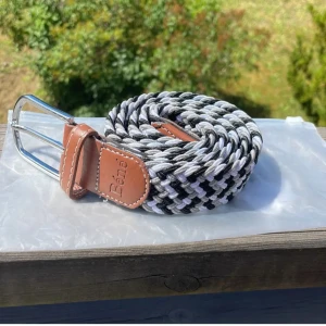 Flätat bälte från Béné - Säljer ett snyggt flätat bälte från Béné i svart, grått och vitt. Bältet har en stilren design med ett brunt läderparti och en silverfärgad spänne. Perfekt för att ge din outfit en cool touch! Passar både till vardags och fest. 🖤🤍