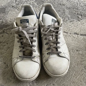 Vita Adidas Stan Smith sneakers - Säljer ett par vita Adidas Stan Smith sneakers i acceptabelt skick. De har en klassisk design med snörning och är tillverkade i skinn. Skorna har synliga tecken på användning, speciellt på sulan och innersulan. Perfekta för en avslappnad stil! Storleken är 38,5. Kan alltid diskutera pris🩷🩷