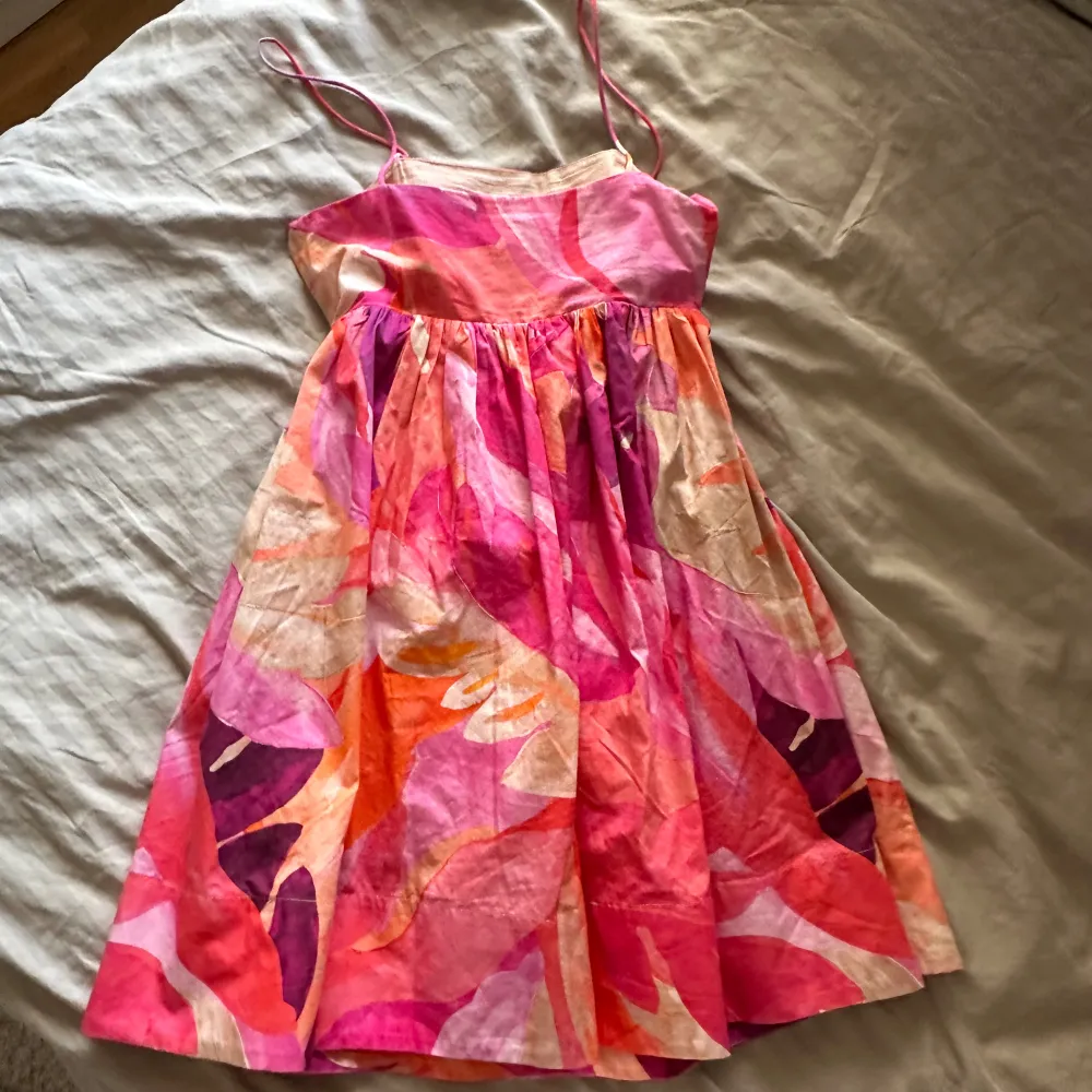 Säljer en superfin sommarklänning i härliga färger som rosa, orange och lila. Klänningen har smala axelband. Perfekt för sommarens alla fester! Den är i mycket bra skick och har en luftig passform som gör den bekväm att bära hela dagen.. Mekot.