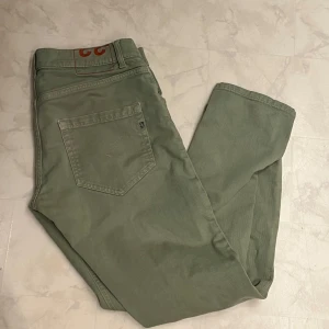 Gröna byxor från Dondup - Säljer ett par snygga gröna byxor från Dondup i storlek 33. De har en klassisk design med knappar och dragkedja framtill. Perfekta för både vardag och lite mer uppklädda tillfällen. Byxorna är i bra skick och har en skön passform.
