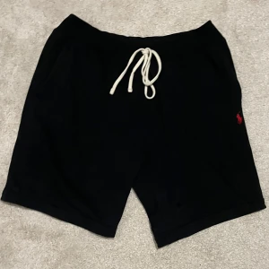 Ralph Lauren shorts - Säljer ett par snygga marinblå (ser svarta ut på bilden bara) shorts från Ralph Lauren i storlek M men passar S bra också. De har en vit snöre i midjan och det klassiska röda Polo-logotypen broderad på sidan. Perfekta för en avslappnad stil i sommar! Ny pris för runt 1000kr
