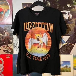 Svart Led Zeppelin T-shirt - Säljer en svart Led Zeppelin T-shirt med tryck från deras U.S. Tour 1975. T-shirten har ett coolt motiv med en ängel i mitten och texten 'Led Zeppelin' i rött och orange. Perfekt för alla rockfans! 🎸dm vid frågor:)