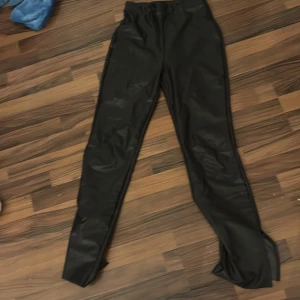 Svarta byxor från NLY Trend - Säljer ett par svarta byxor från NLY Trend i storlek S. Byxorna har en sleek och stilren design, perfekt för både vardag och fest. De är tillverkade i ett syntetmaterial som ger en glansig finish. Passar bra till en chic outfit!
