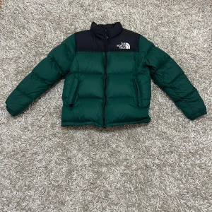 Grön och svart dunjacka från The North Face - Säljer en snygg och varm dunjacka från The North Face i grönt och svart. Storlek XL junior med passar XS Jackan har en dragkedja framtill och är perfekt för kalla vinterdagar. Den är i mycket bra skick och har långa ärmar. Perfekt för dig som vill hålla stilen i vinter! ❄️(Pris kan diskuteras)